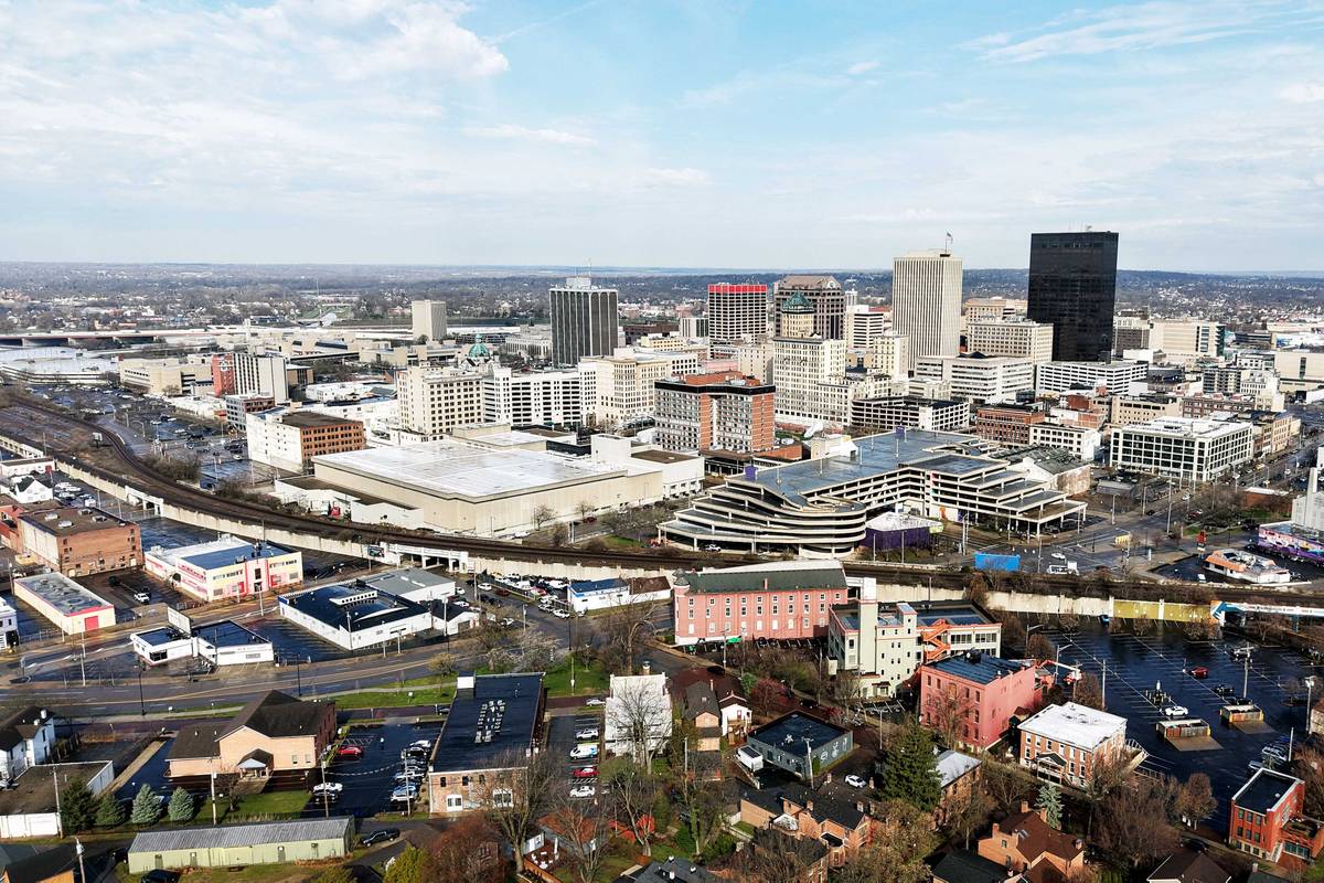 Aerial view over Dayton, Ohio, with the downtown core in the middle distance beyond low-rise blocks and a rail corridor.